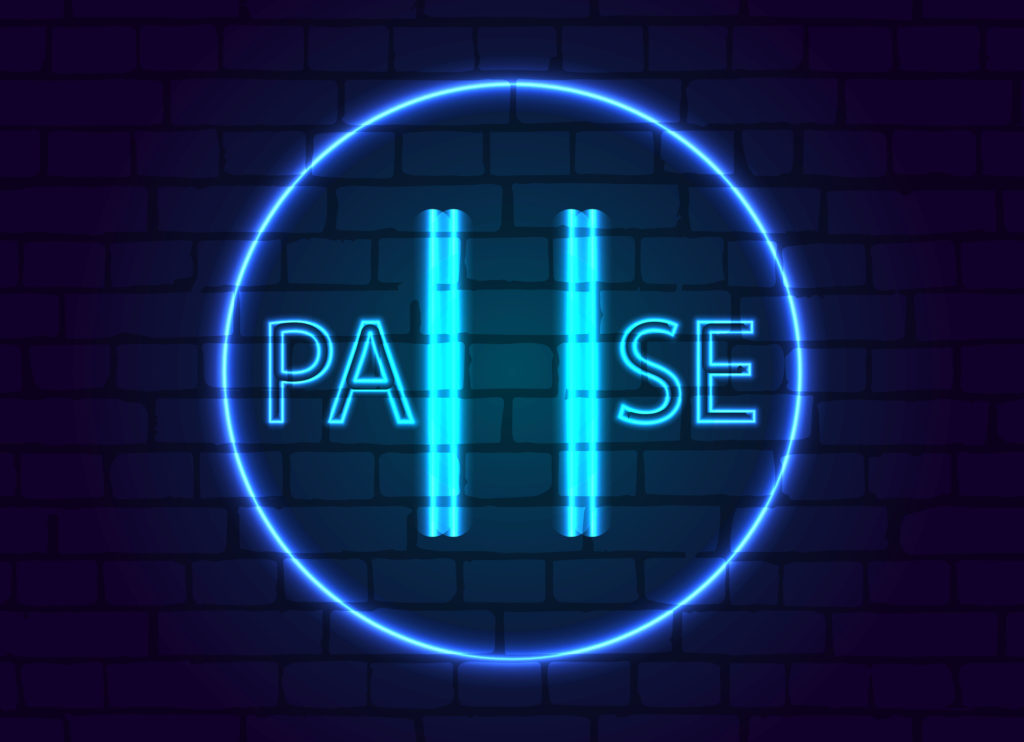 Pause Sign in a neon blue on a brick wall in the dark